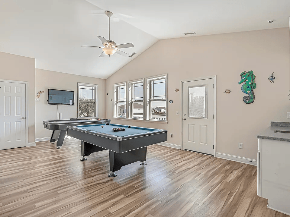 Bright game room with a pool table, wood floors, ceiling fan, and wall-mounted TV
