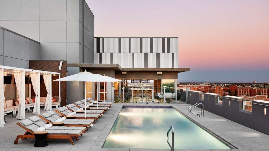 Rooftop pool with lounge chairs and a view of a city skyline at dusk.