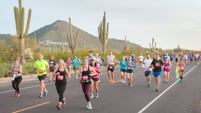 Runners on a road in the desert, Saguaro cacti and Phoenix sign in the background.