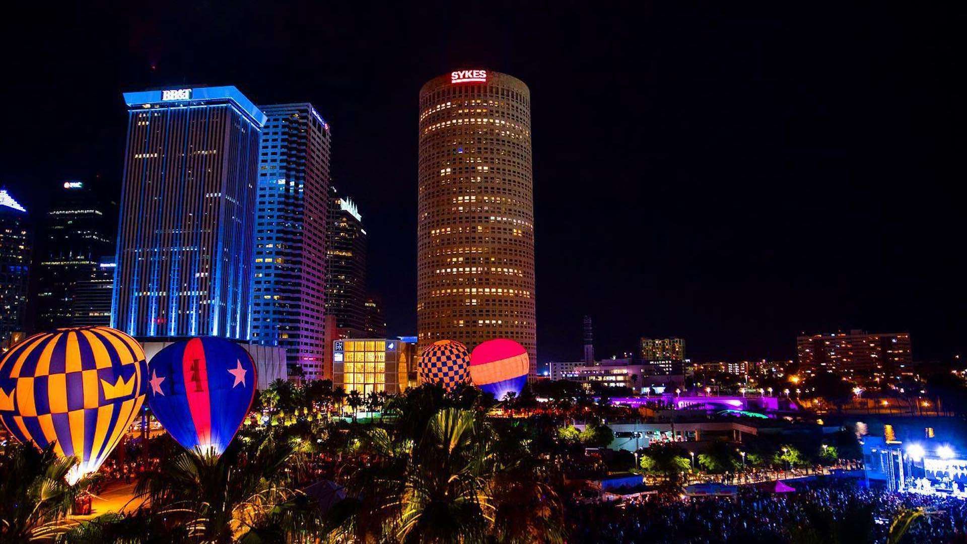 Night view of Tampa, Florida skyline with hot air balloons and brightly lit buildings.