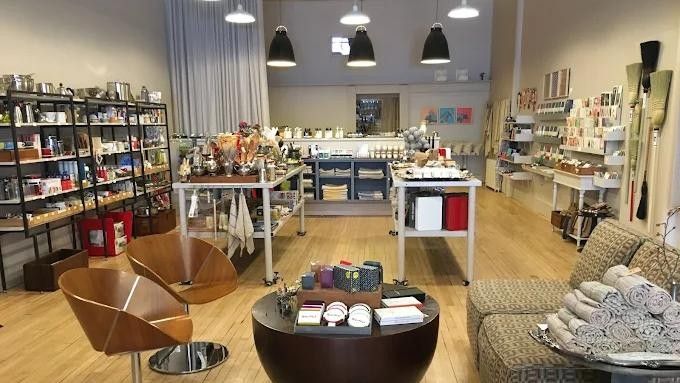 Interior of a shop with shelving, tables, chairs, and various products for sale, including personal care items and home goods.
