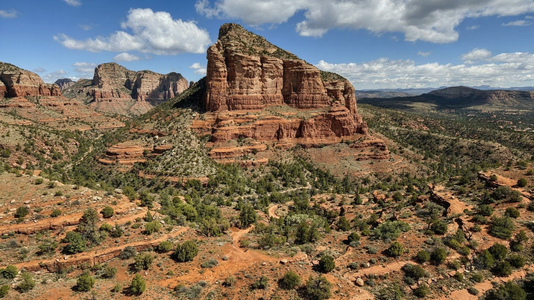 Red sandstone buttes and mesas rise above a sparse desert landscape under a bright blue sky.