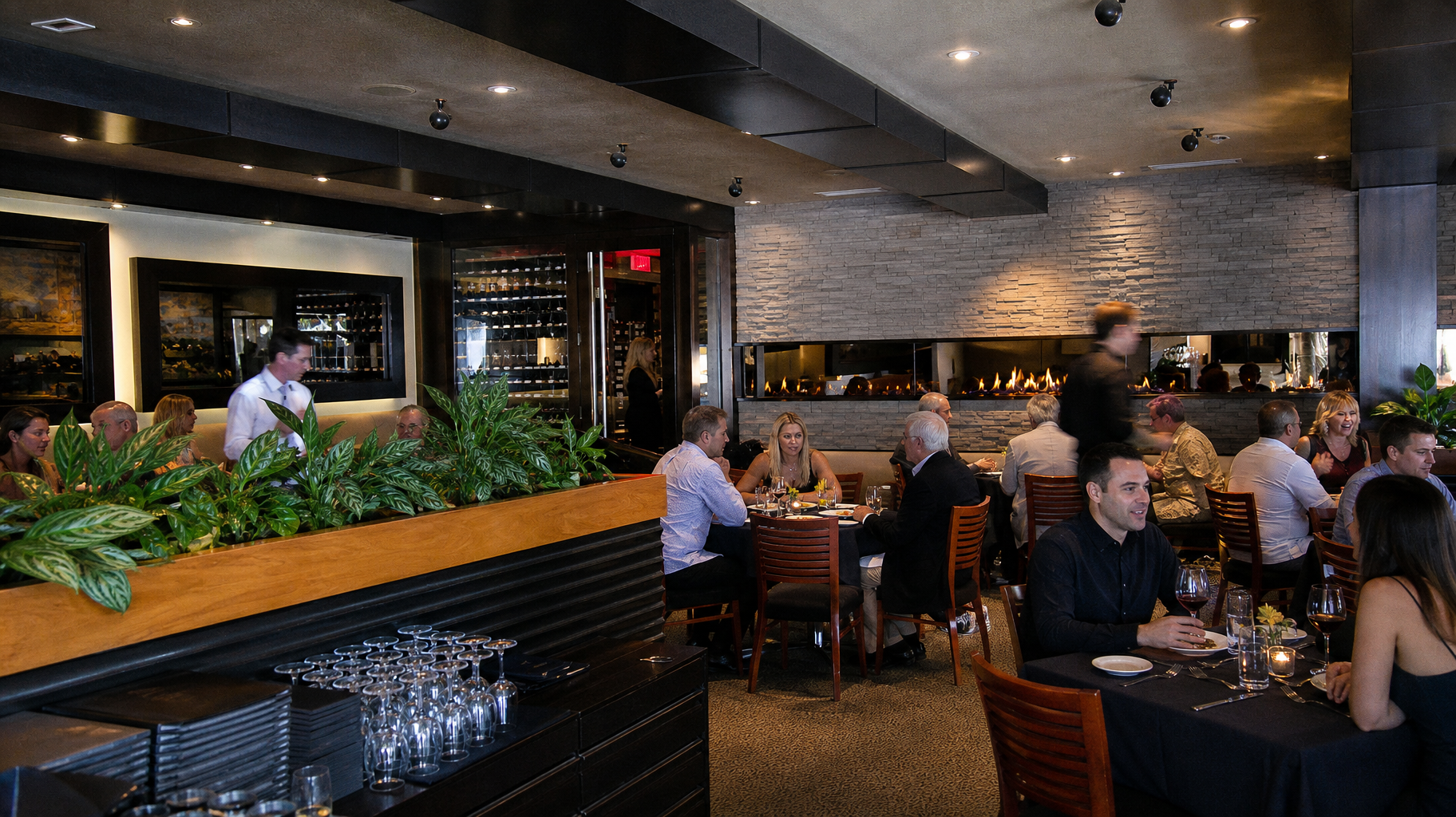 Busy modern restaurant dining room with people seated at tables under warm lighting and brick walls