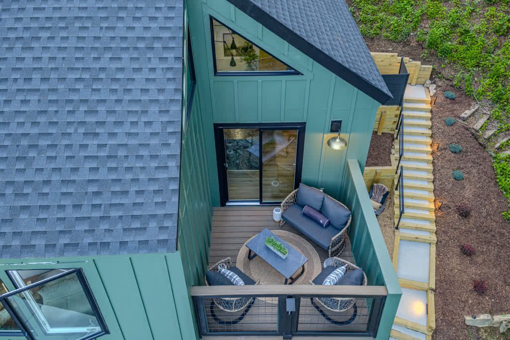 Aerial view of a teal house balcony with outdoor seating and lights beside a garden path