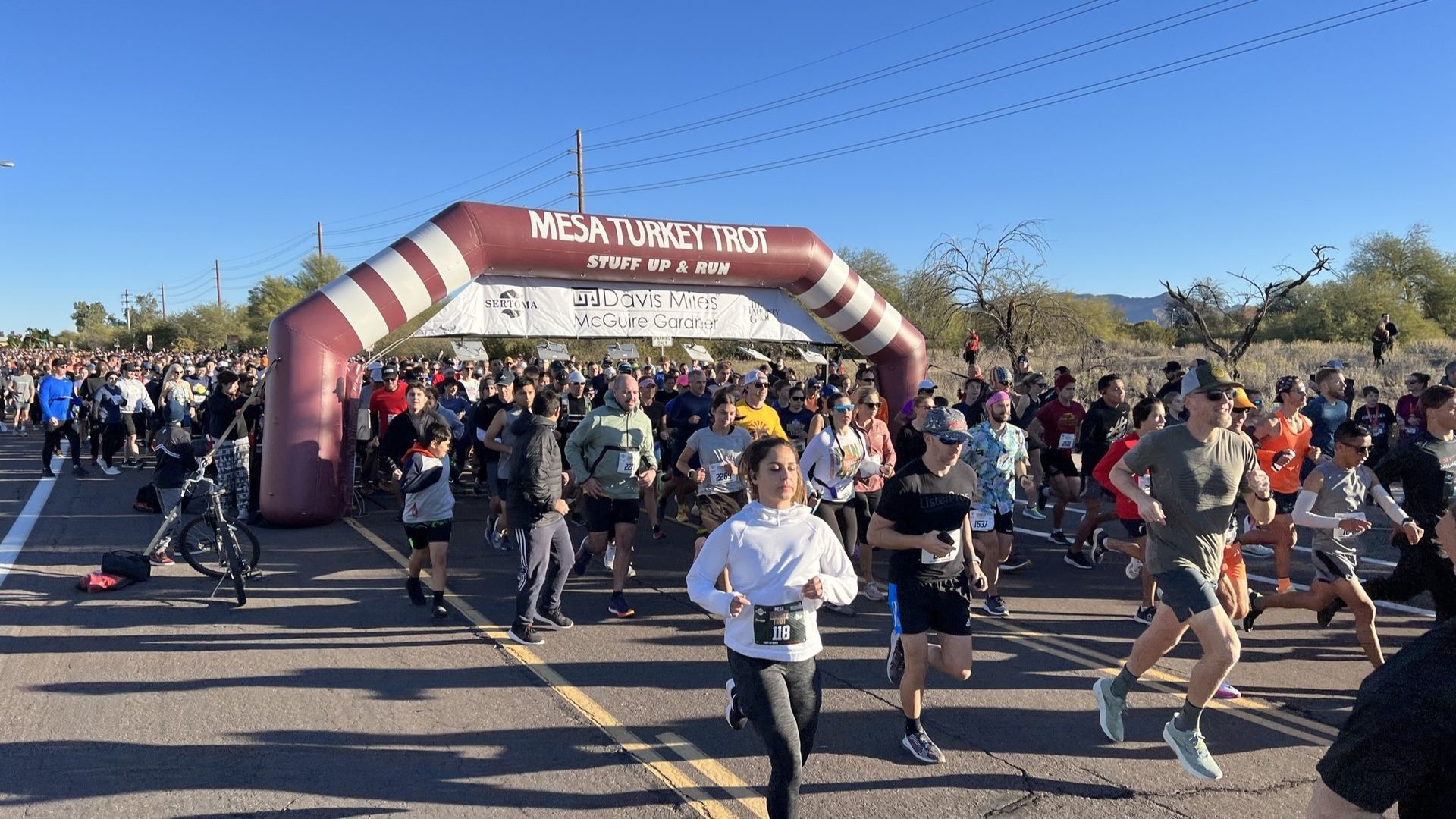 Runners at the start of the Mesa Tropical Hike, under an inflatable archway. Road lined with participants.