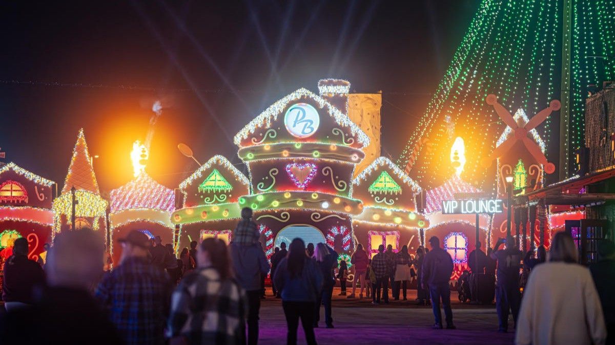 Holiday lights display with buildings, trees, and crowd of people at night.