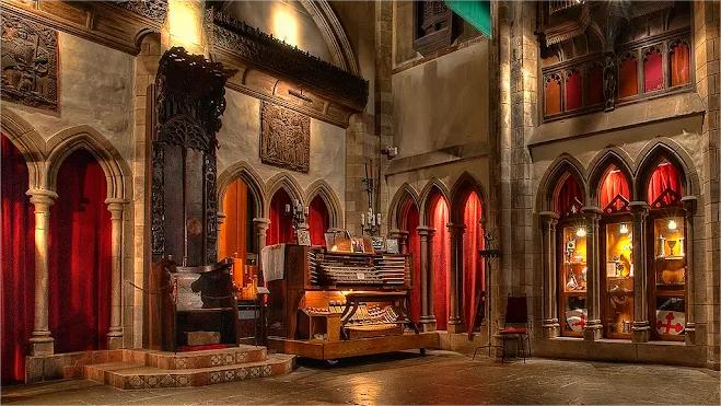 Ornate, gothic-style room with red curtains, arched windows, and a large wooden organ.