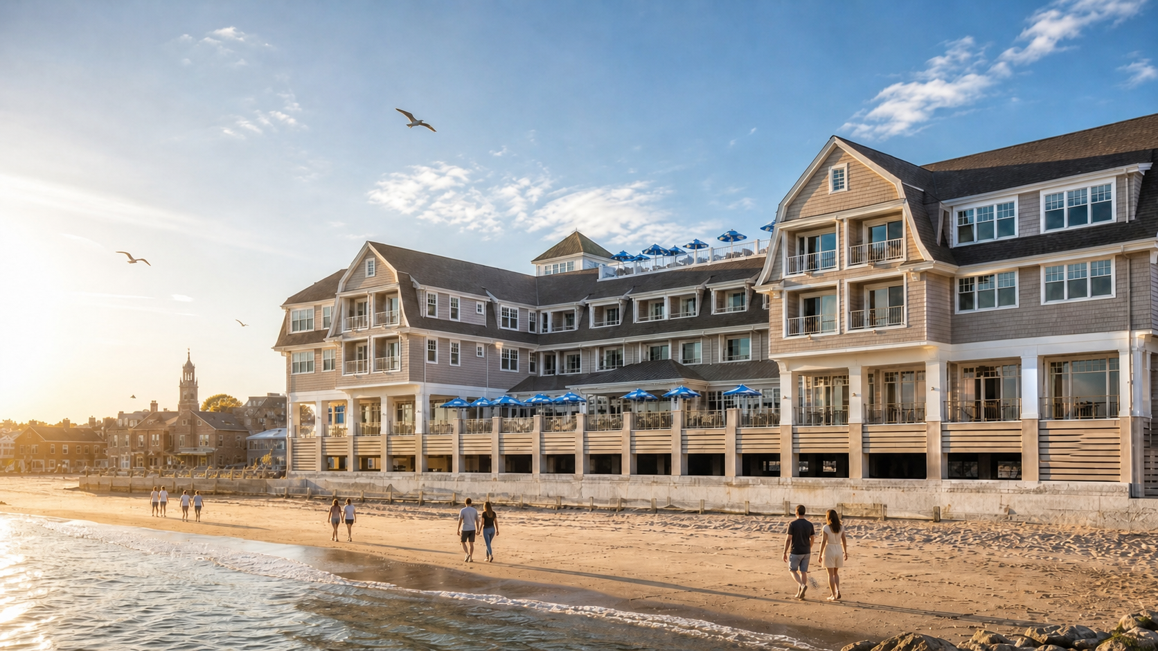 Sunlit beachfront resort building with people walking on the sand by the water