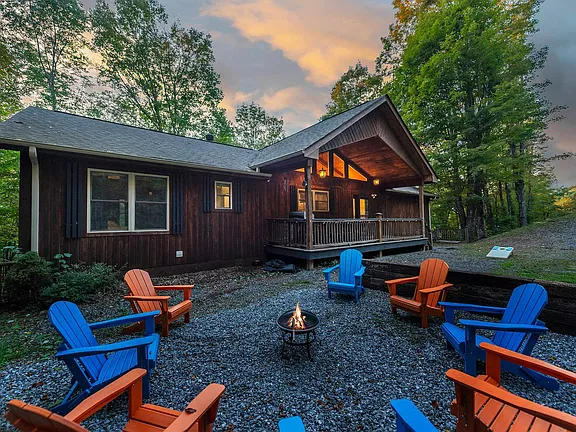 Cabin patio with blue and orange chairs around a fire pit at sunset, surrounded by trees