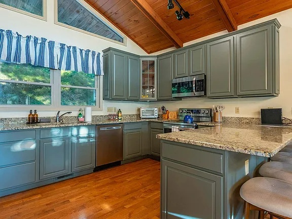 Bright kitchen with gray cabinets, granite counters, wood ceiling, and blue curtains over a window.