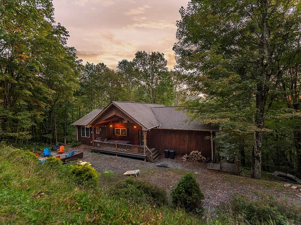 Rustic cabin at dusk in a wooded clearing, with warm porch lights and kayaks by the shore