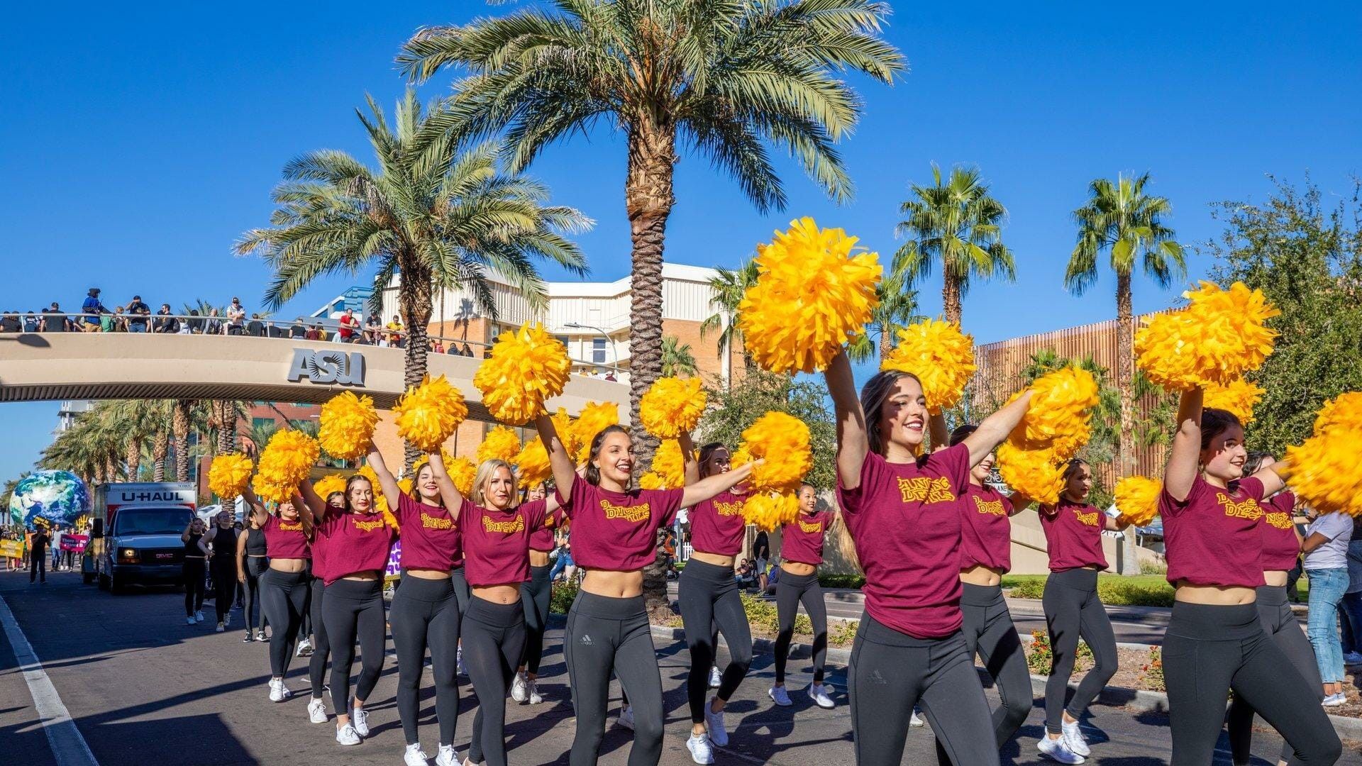 Arizona State cheerleaders in maroon and gold perform with pom-poms during a parade.