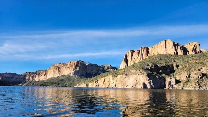 Lake with rocky cliffs under a bright blue sky.