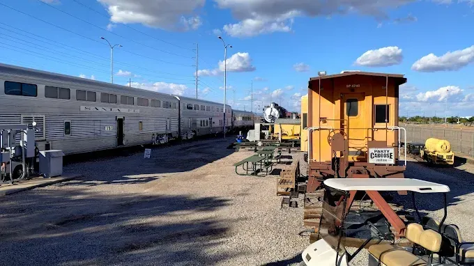 A train and a yellow caboose in a rail yard under a blue sky with utility poles.
