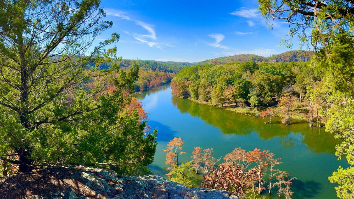 River winds through a lush, forested valley under a bright blue sky.