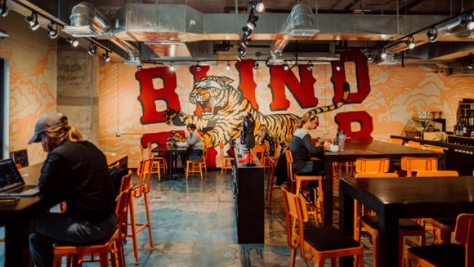 Interior of a cafe with a tiger mural, people sitting at tables, and exposed ceiling.