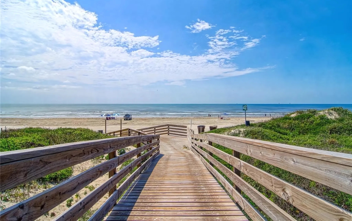 A wooden walkway leading to the beach with a view of the ocean in Port Aransas, Texas