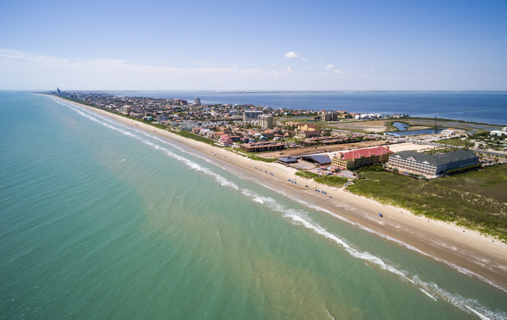 An aerial view of a long beach with a city in the distance in South Padre Island, Texas