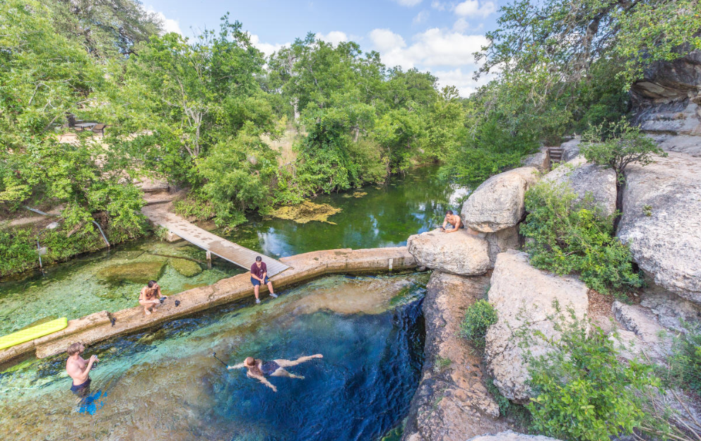 A group of people are swimming in a lake surrounded by trees in Wimberley, Texas