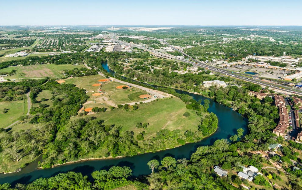 An aerial view of a river surrounded by trees and a city in New Braunfels, Texas