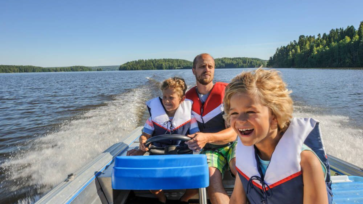 Man and two children ride in a motorboat on a lake; all wearing life vests.