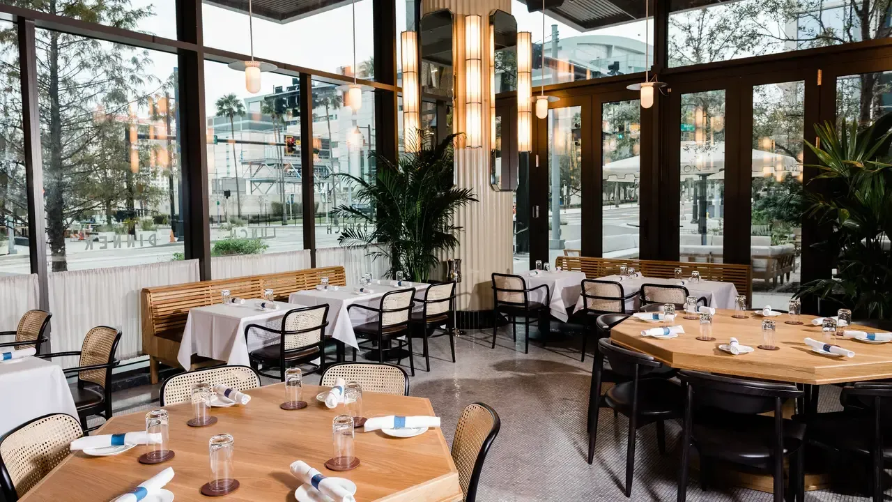 Restaurant interior with tables set for dining, surrounded by large windows.