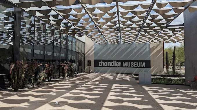 Chandler Museum entrance under a patterned shade structure. Glass building, sign, shadows.