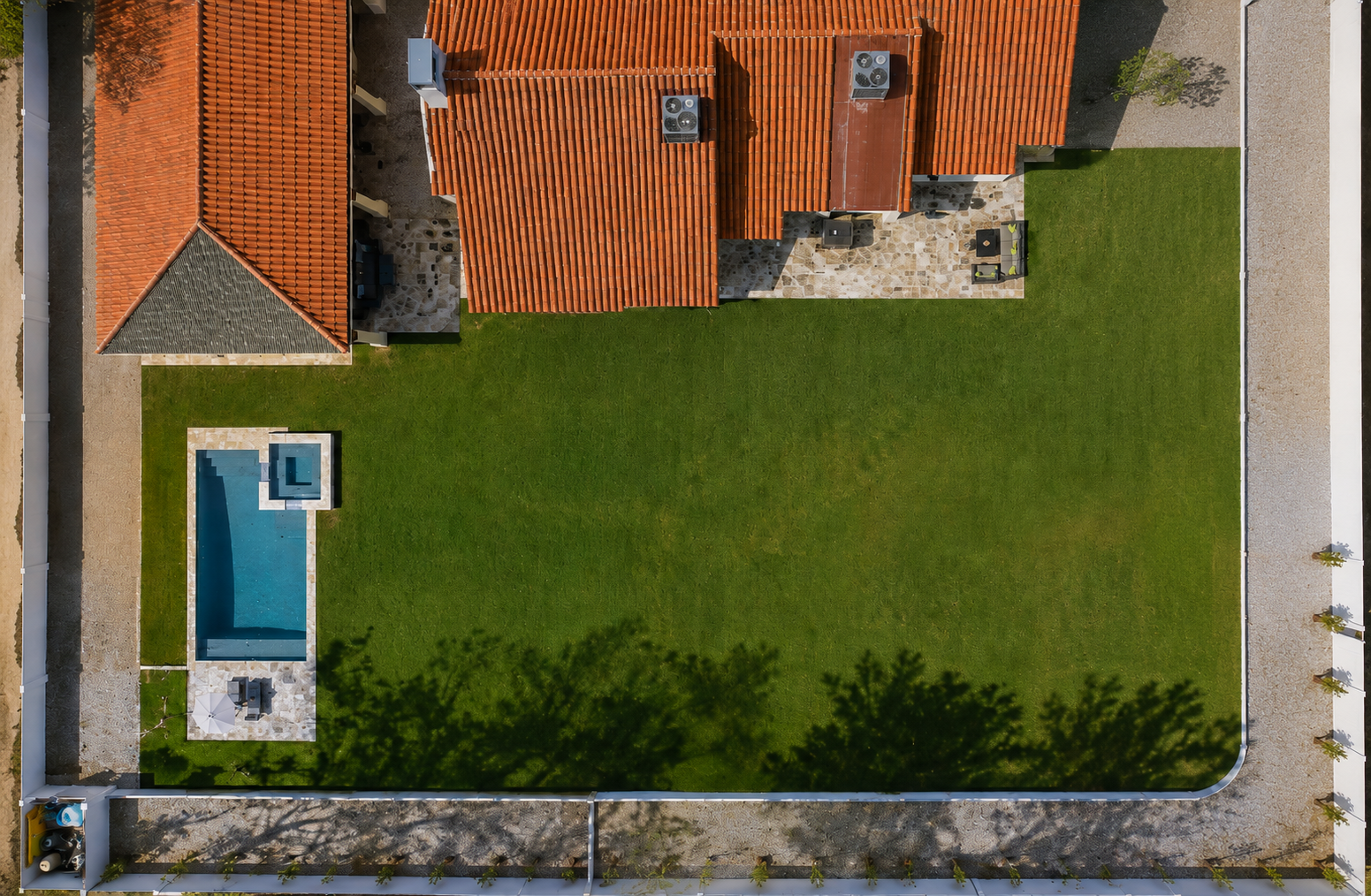 Aerial view of a house with red tile roof, green lawn, and a small blue pool in the corner.