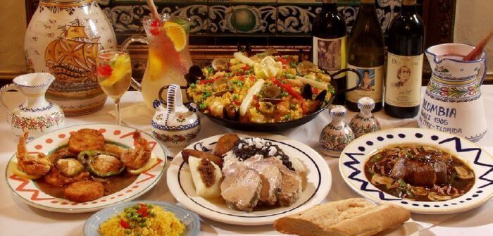A table laden with Spanish food: paella, seafood, meat dishes, bread, and drinks.