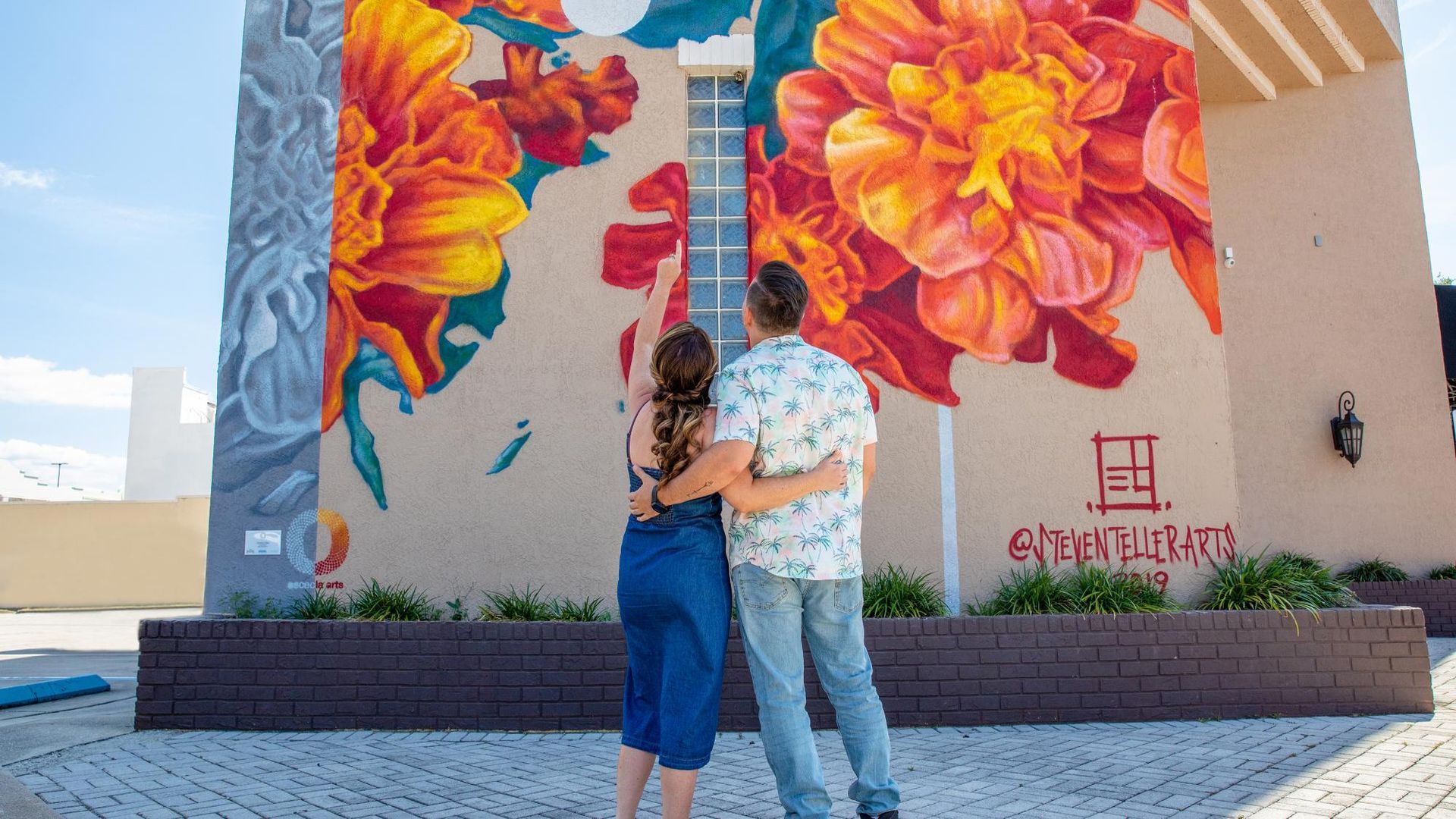 Couple admiring a vibrant floral mural on a building's exterior.