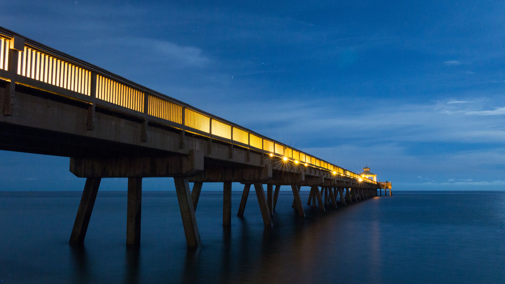 A pier in Deerfield Beach, FL is lit up at night and going into the ocean.