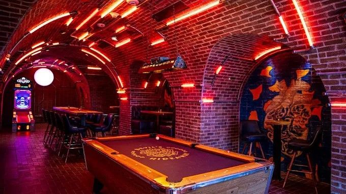 Pool hall with brick walls, arched ceiling, neon red lights, and a pool table.