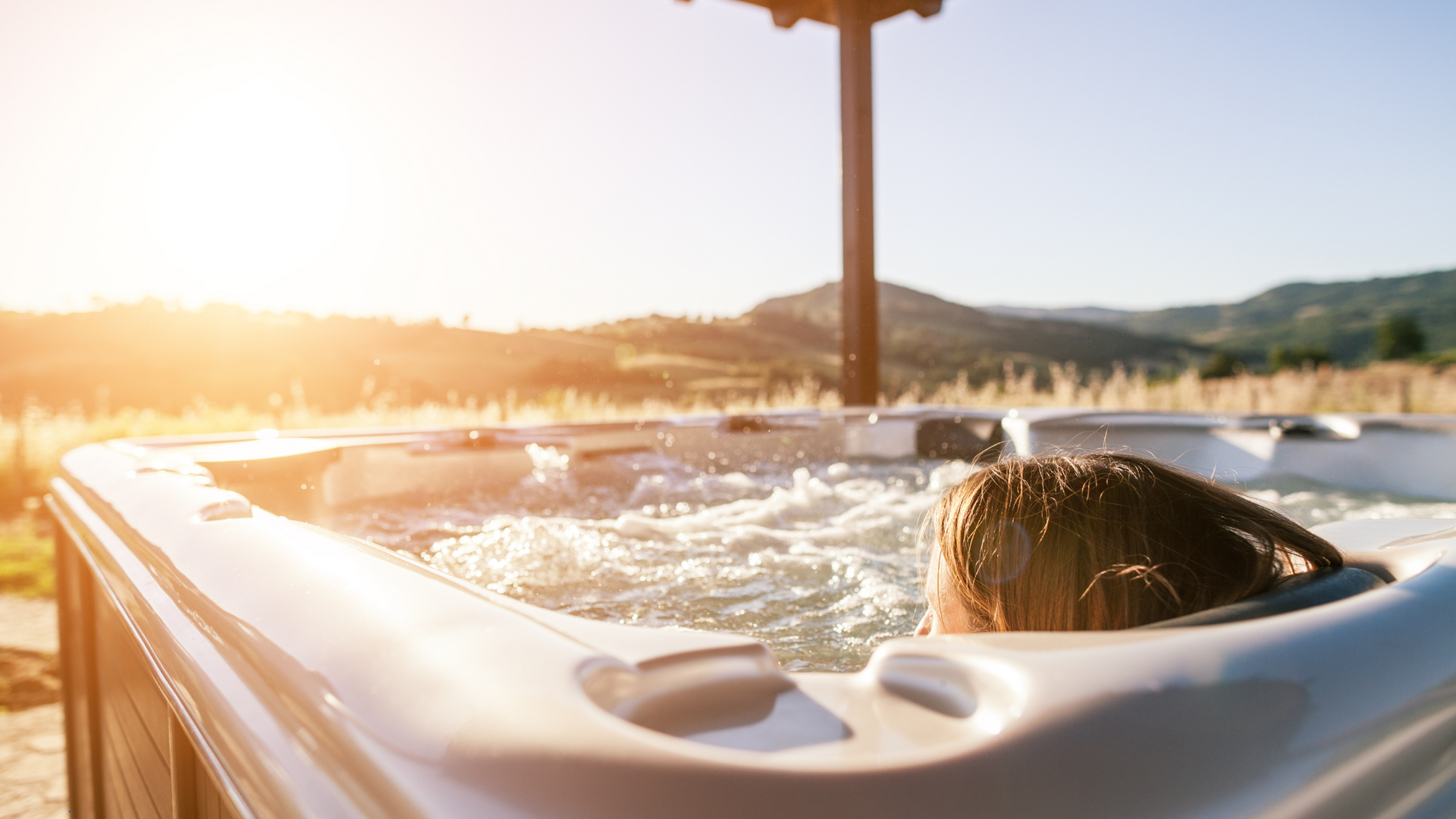 A woman is sitting in a hot tub with mountains in the background.