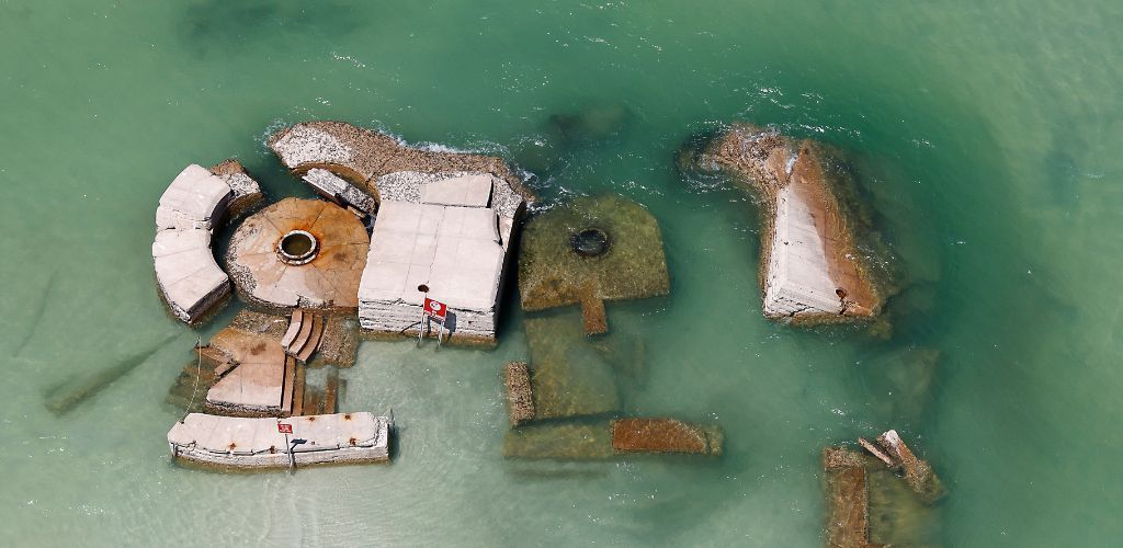 Aerial view of partially submerged concrete structures in clear turquoise water.