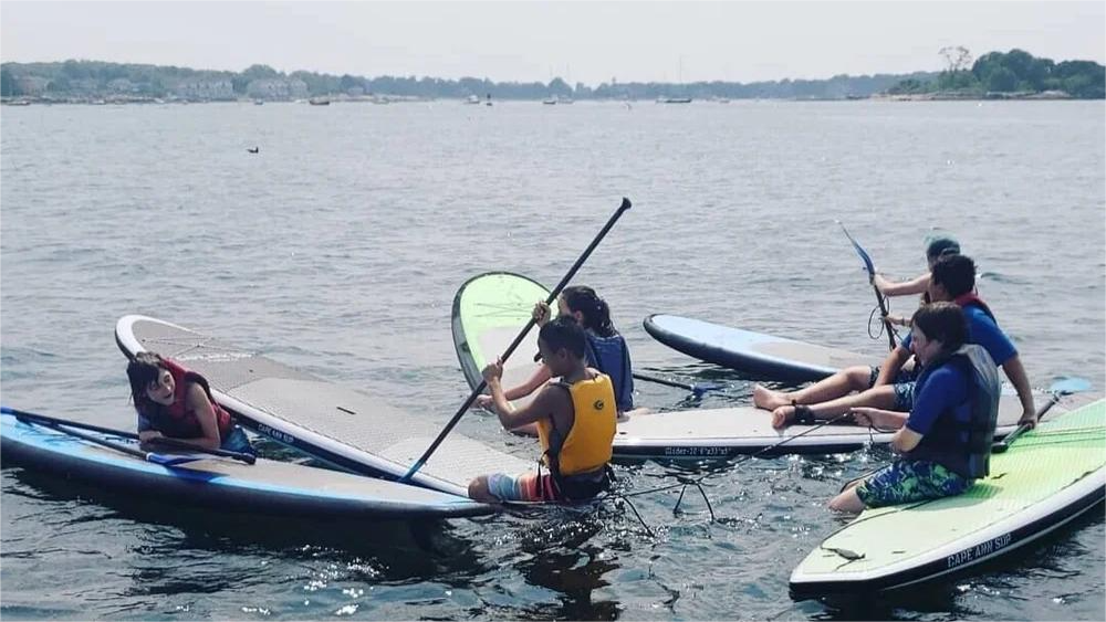 People paddleboarding on a body of water; some are sitting, and one is using the paddle.