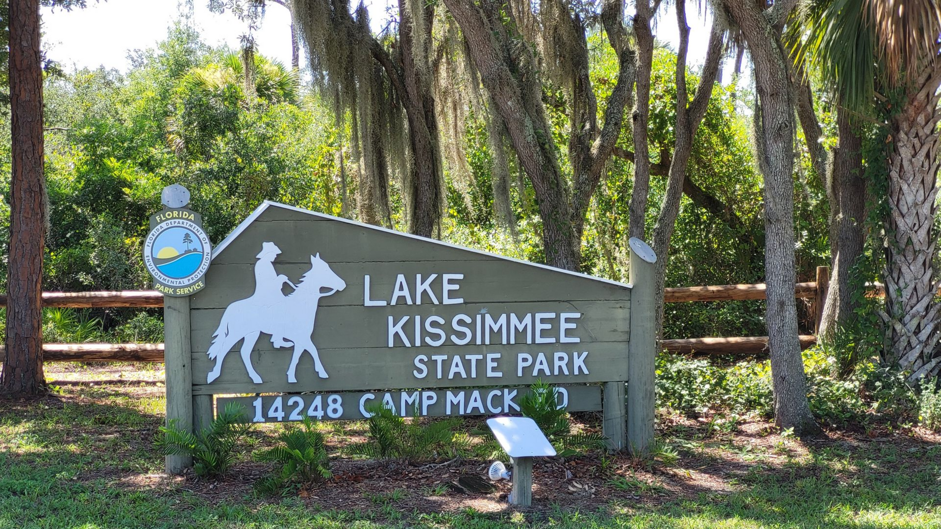 Sign for Lake Kissimmee State Park with a horse and rider silhouette, near trees.