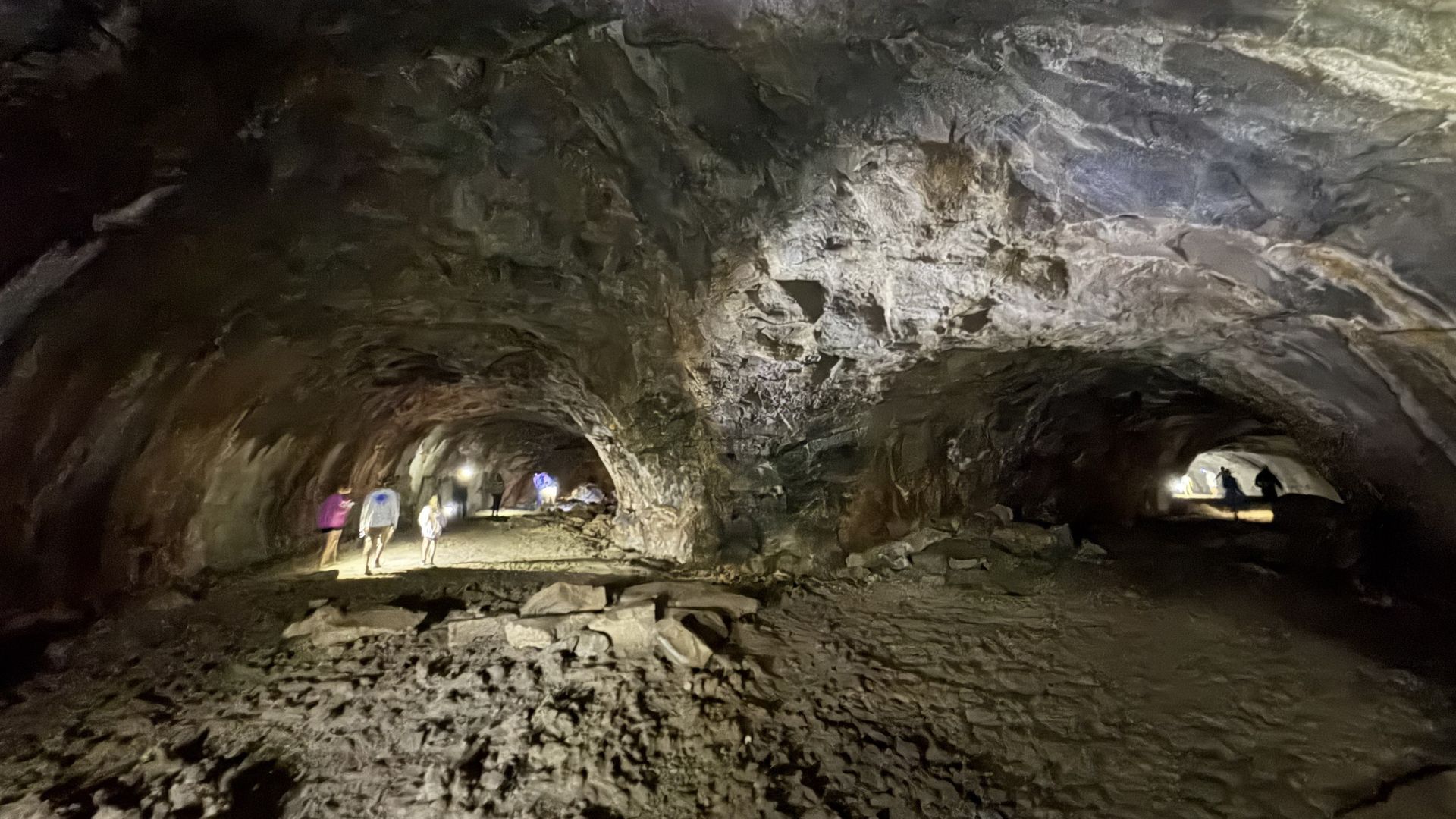 People walking in a dark lava cave. Illuminated tunnel with rock walls and ceiling.