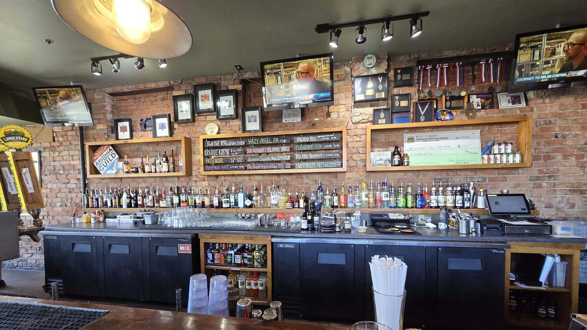 Bar with bottles, glasses, and a cash register on a brick wall background.