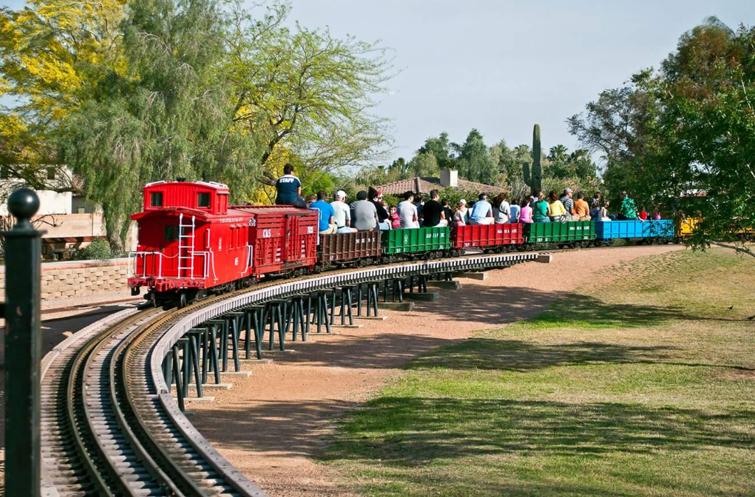 A small train, filled with kids and adults alike, is going down the tracks in McCormick-Stillman Railroad Park