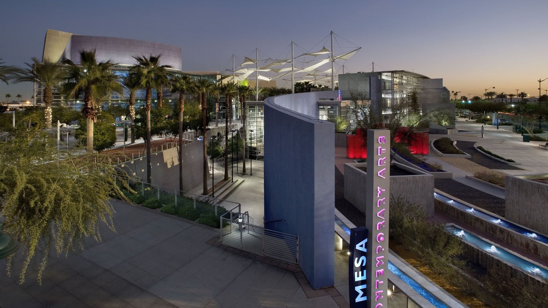 Mesa Arts Center exterior at dusk with palm trees, walkways, and modern buildings.