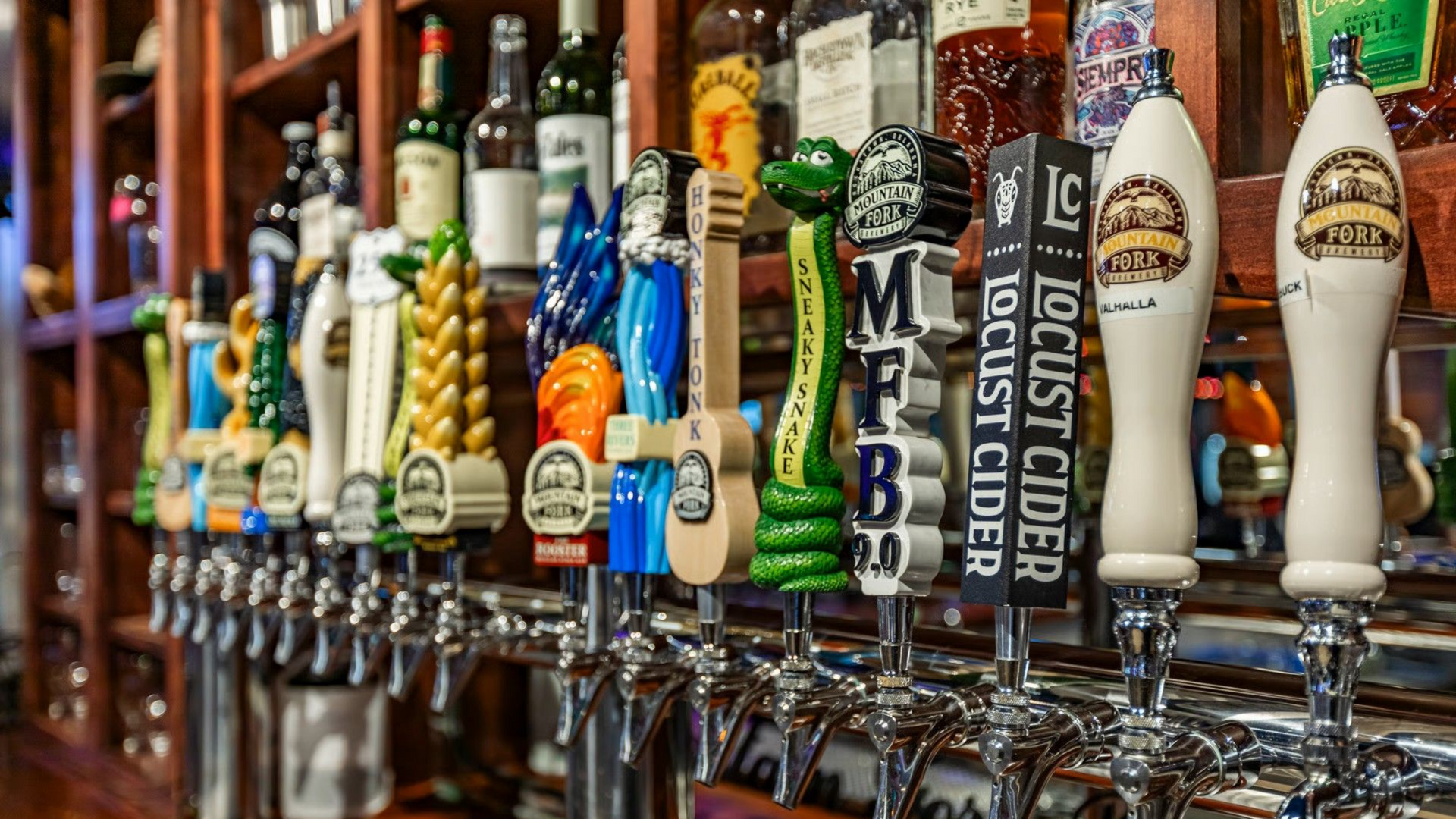 Close-up of beer taps with decorative handles at a bar, bottles on shelves in the background.