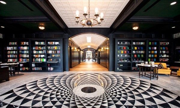 Library interior with dark shelving, arched hallway, and black/white geometric floor pattern.