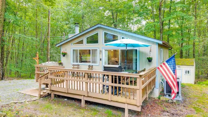 Cottage with wooden deck, American flag, and trees. The deck has a patio umbrella.