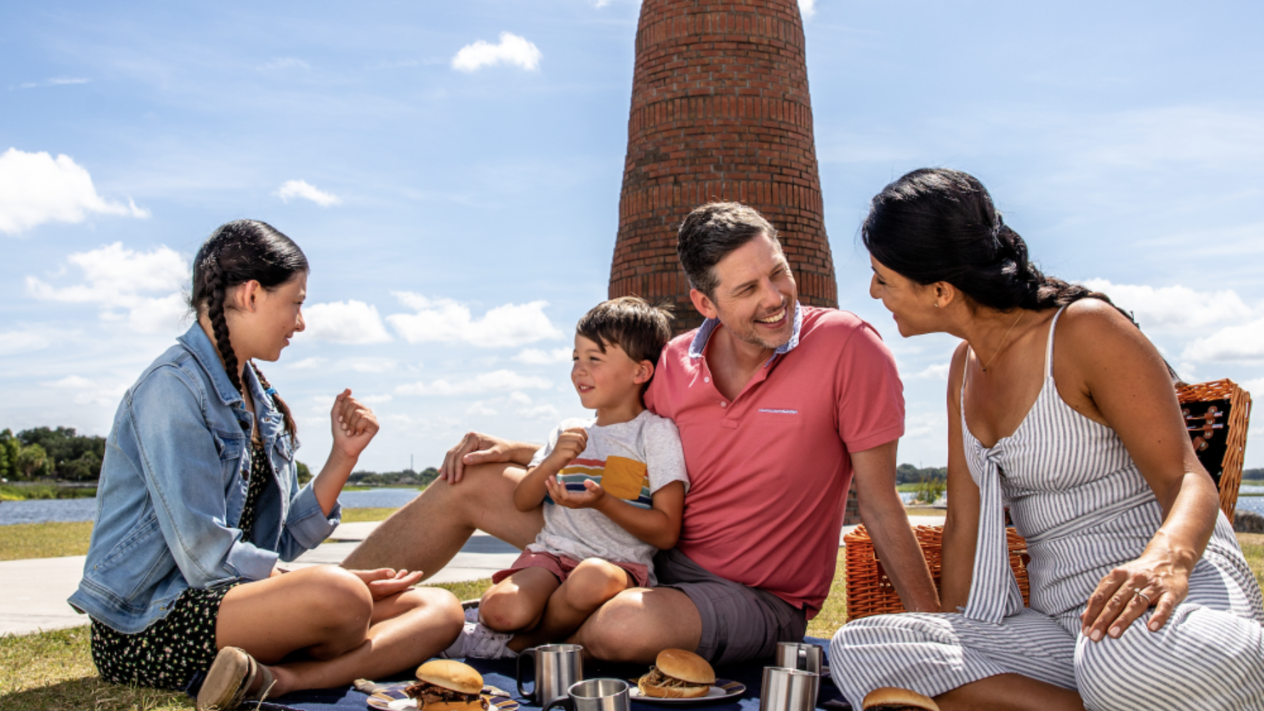 Family picnicking near a tall brick structure, sunny day.
