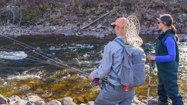 Two people fly fishing in a river; man in grey shirt, woman in blue and green waders.