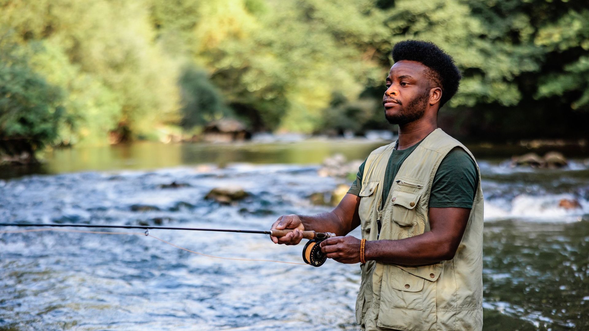 Man fishing in a river, wearing a vest.
