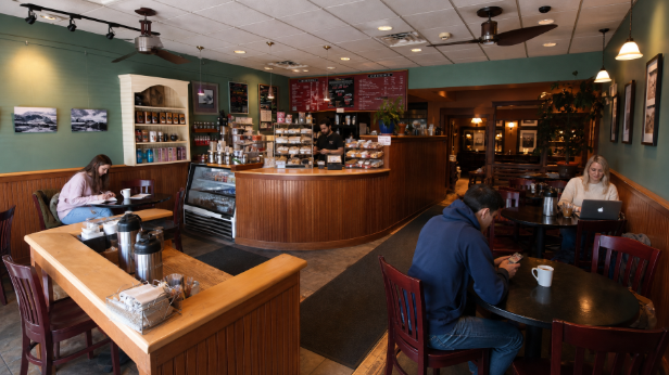 Cozy café interior with a curved wooden bar, tables, and a few patrons seated near the windows.