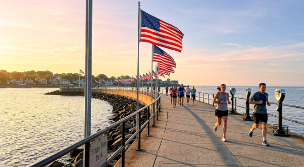 Sunset on a waterfront walkway with several people jogging and large American flags waving