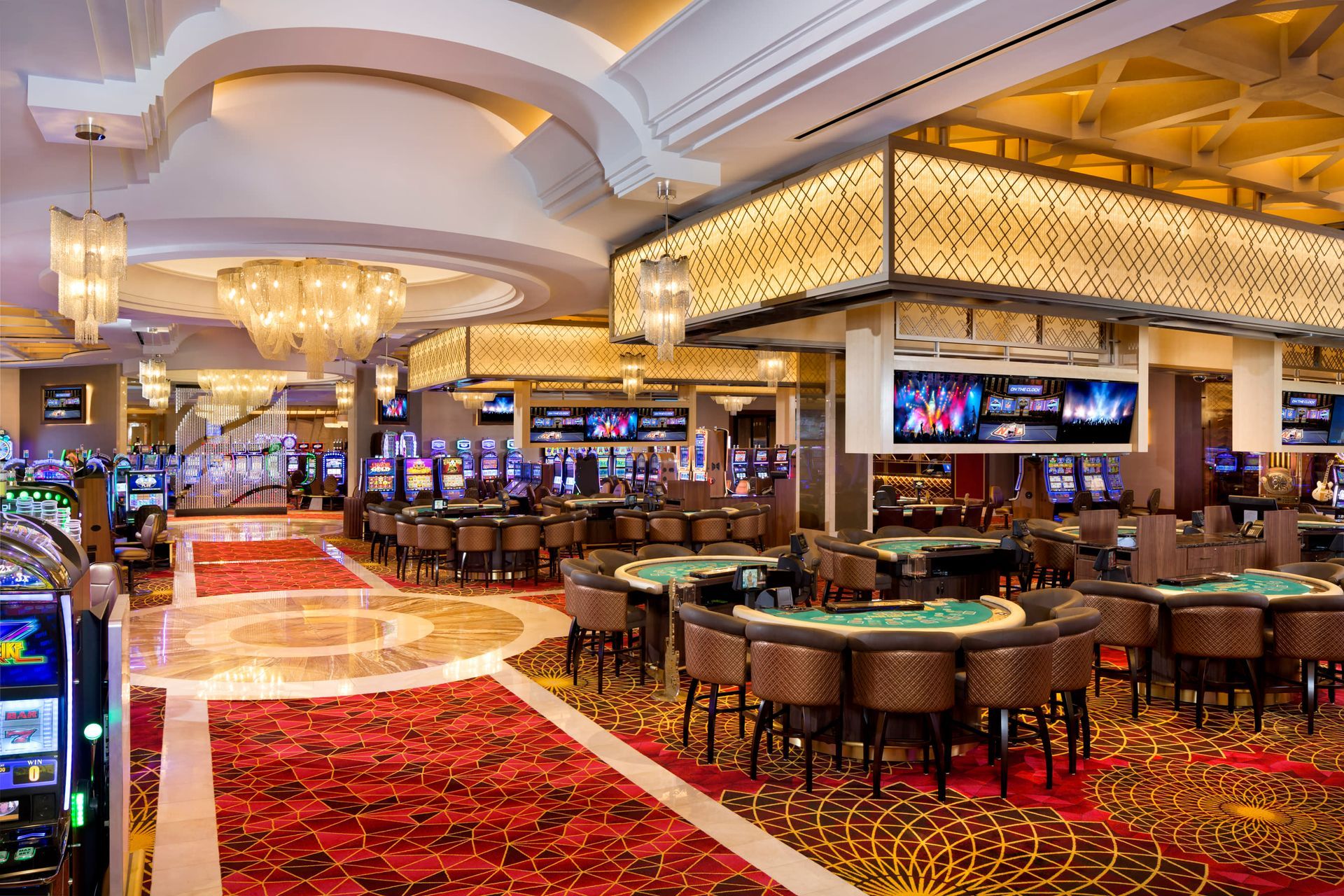 Casino interior with slot machines, table games, and ornate decor, including a red carpet and chandeliers.