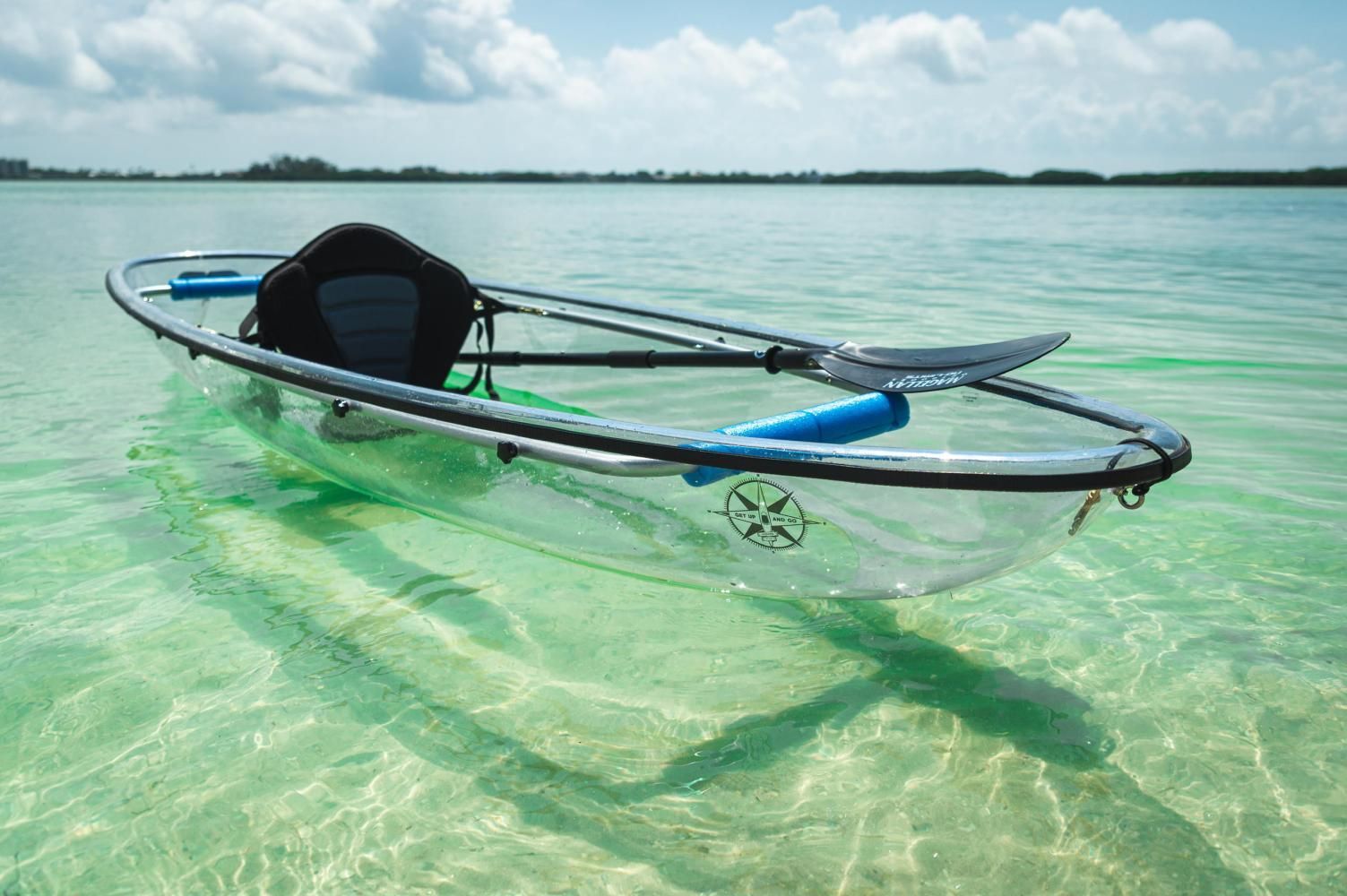Clear kayak on turquoise water with paddle, black seat, and blue accents.